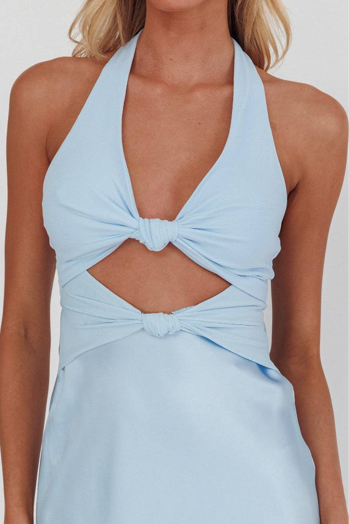 A woman wearing a light blue halter-neck dress with a twisted knot detail at the bust and waist, shown against a plain light gray background.