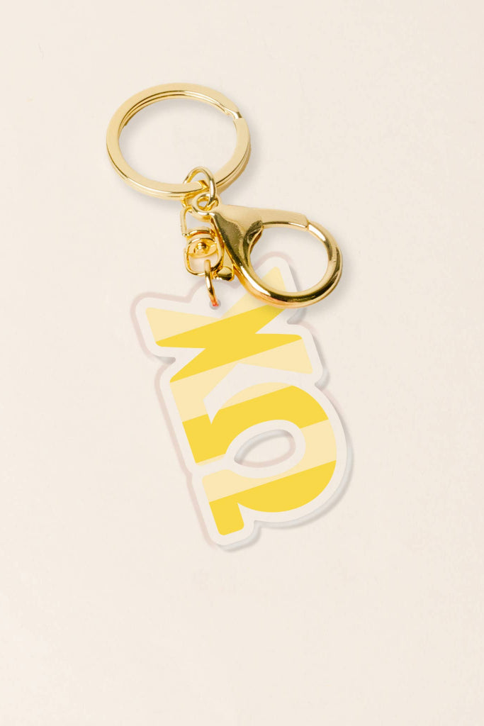 Keychain with yellow 'KP' letters on a beige background