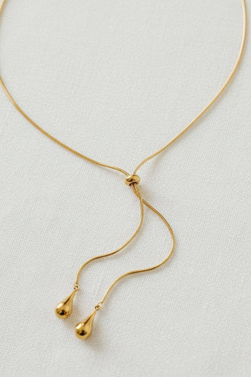 Gold necklace with teardrop pendants on a light gray background