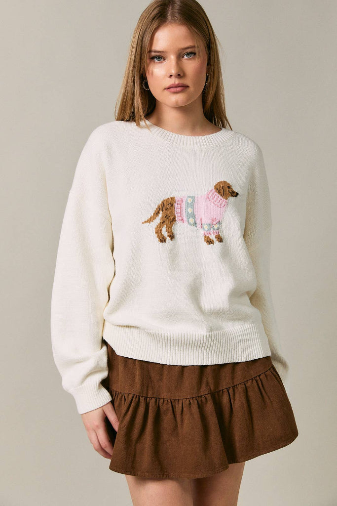 Woman wearing a cream sweater with a dog design and a brown skirt on a plain background