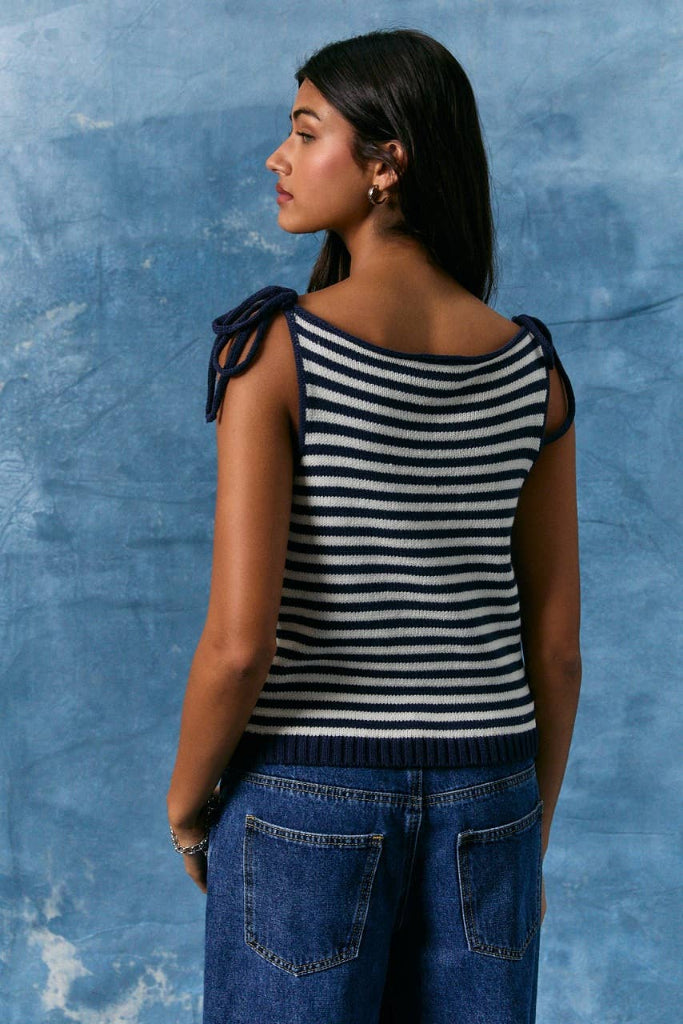 Woman wearing a navy and white striped sleeveless top against a blue textured wall.