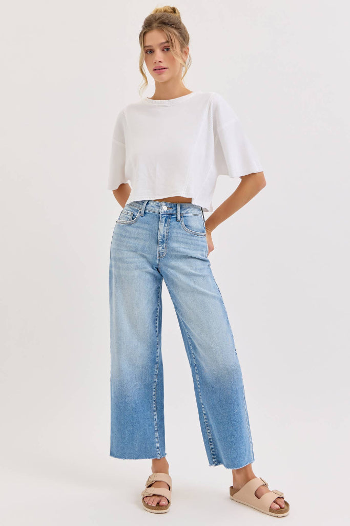 Woman wearing a white cropped top and light blue jeans on a white background