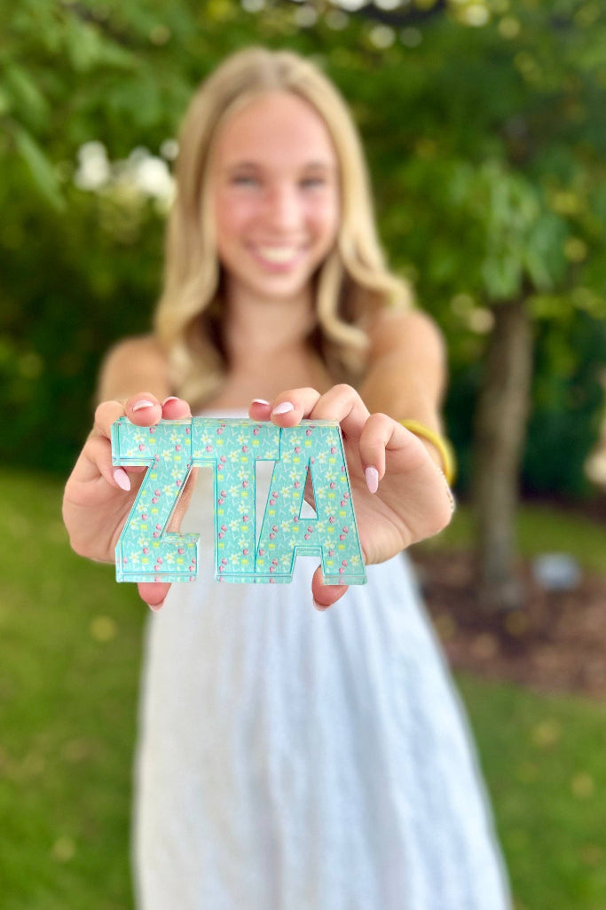 Woman holding 'ZITA' letters outdoors with greenery in the background