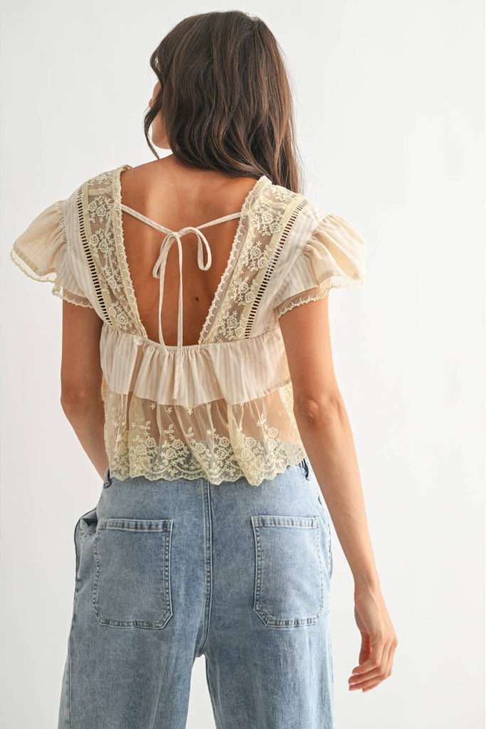 Woman wearing a lace top with an open back and light blue jeans on a white background