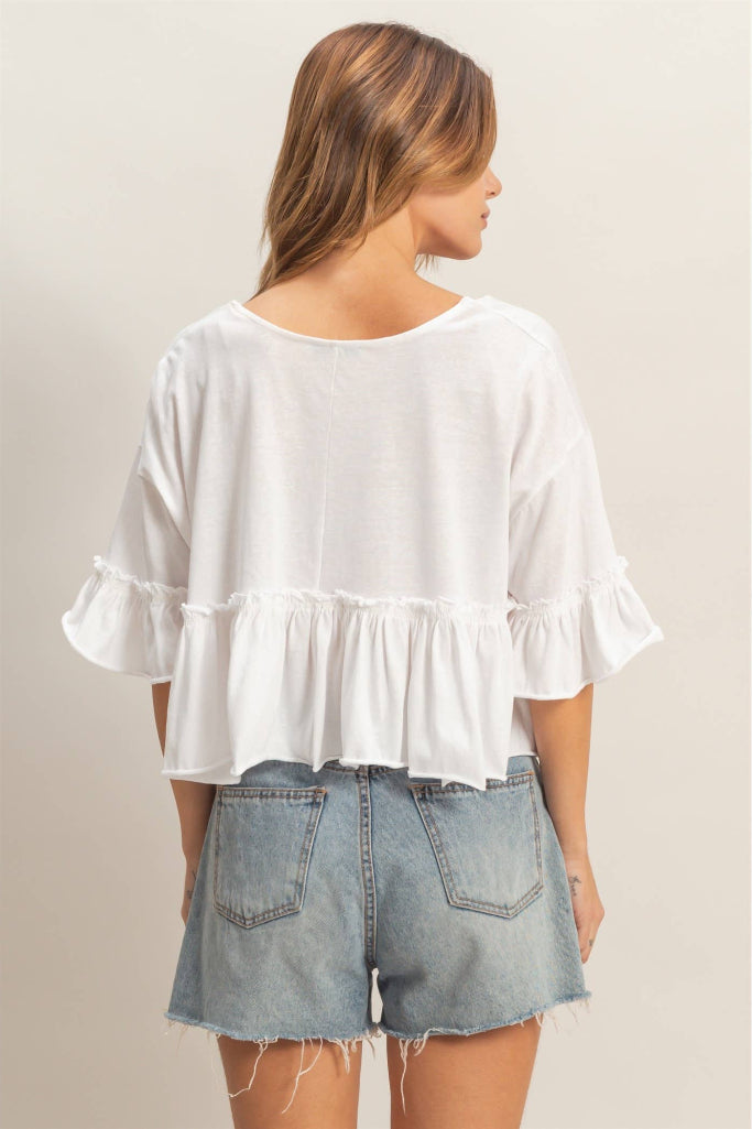 Woman wearing a white blouse with ruffled sleeves and denim shorts on a plain background