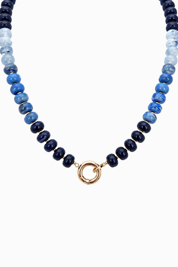 A beaded necklace featuring alternating strands of polished dark navy, medium blue, and light blue beads, finished with a central gold-tone split ring clasp, shown against a plain white background.
