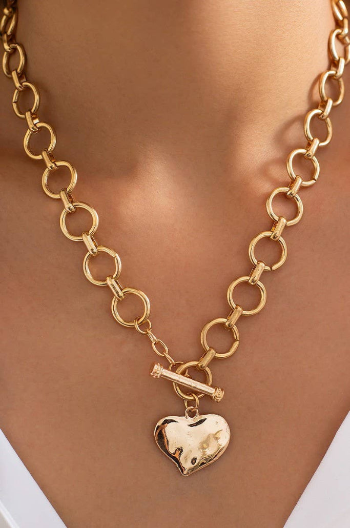 Gold chain necklace with a heart-shaped pendant on a person's neck.