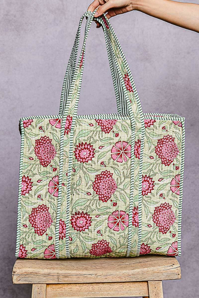 Floral patterned tote bag held by a hand against a gray background