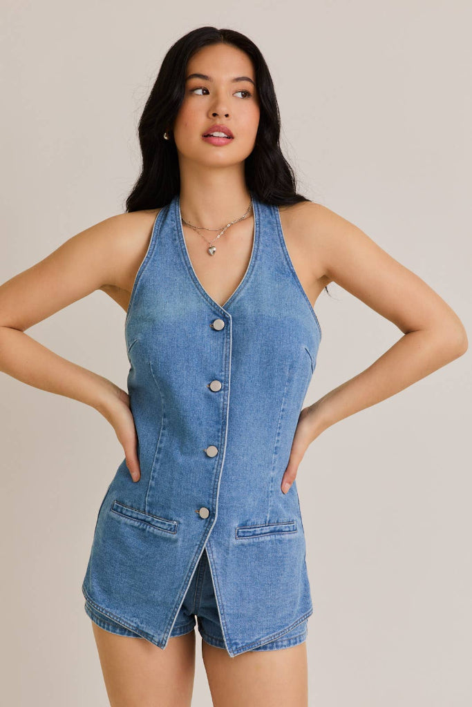 Woman wearing a denim romper with brown boots on a plain background