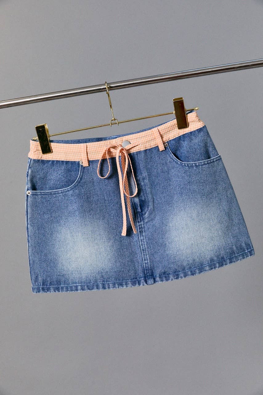 Blue denim skirt with a pink belt on a gray background