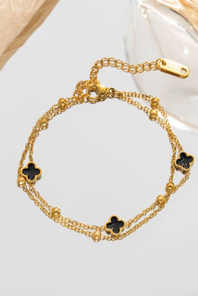 Gold bracelet with black flower-shaped charms on a light background
