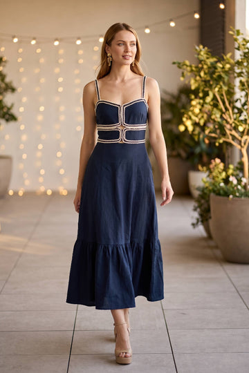 Woman wearing a navy dress with white patterns in an outdoor setting with plants and string lights.