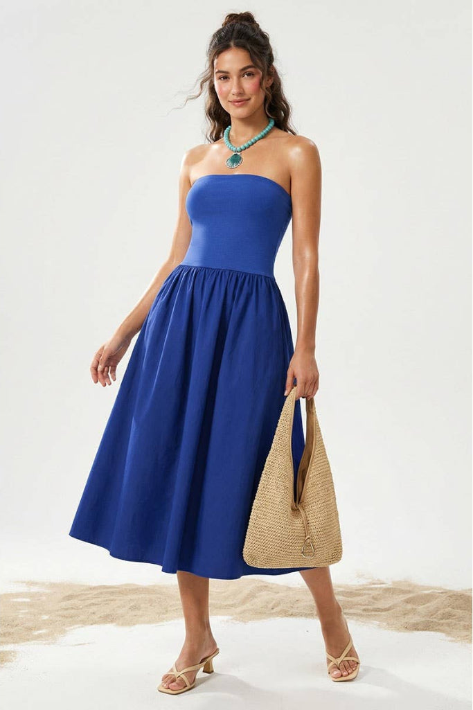 Woman wearing a blue strapless dress holding a straw bag on a white background