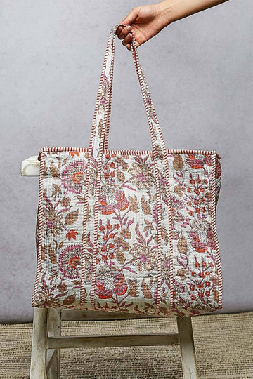 Floral patterned tote bag held by a hand against a gray background