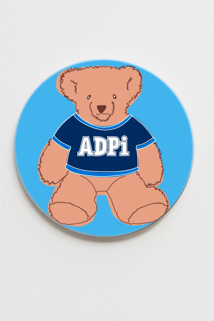 Round blue coaster with a teddy bear wearing a blue shirt with 'ADPI' on a white background