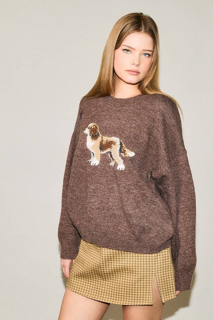 A woman modeling a brown knit sweater featuring a dog graphic on the front, paired with a yellow and brown checkered mini skirt, against a plain light gray background.