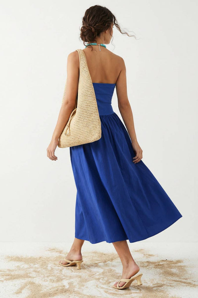 Woman wearing a blue strapless dress holding a straw bag on a white background