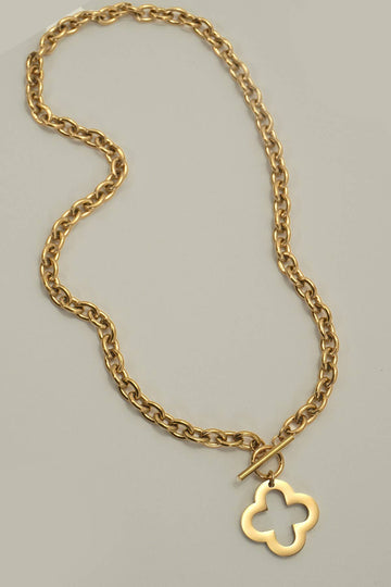A gold chain necklace with a toggle clasp and a small openwork four-leaf clover pendant, photographed on a plain light gray background.