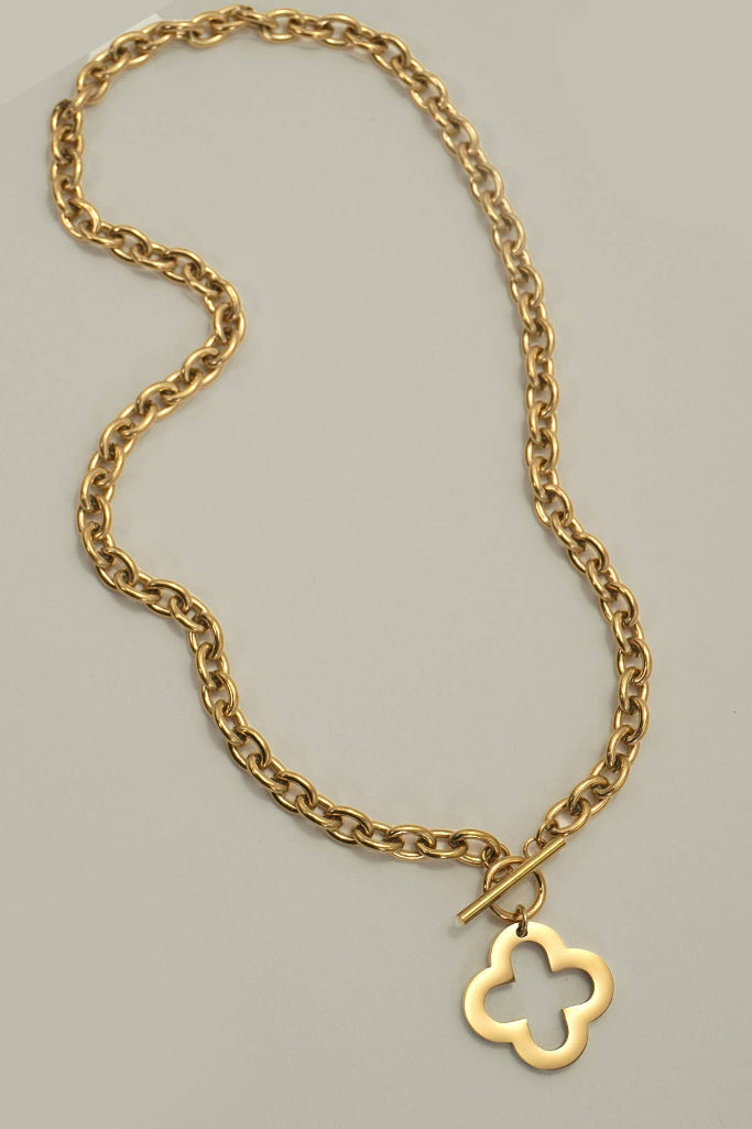 A gold chain necklace with a toggle clasp and a small openwork four-leaf clover pendant, photographed on a plain light gray background.