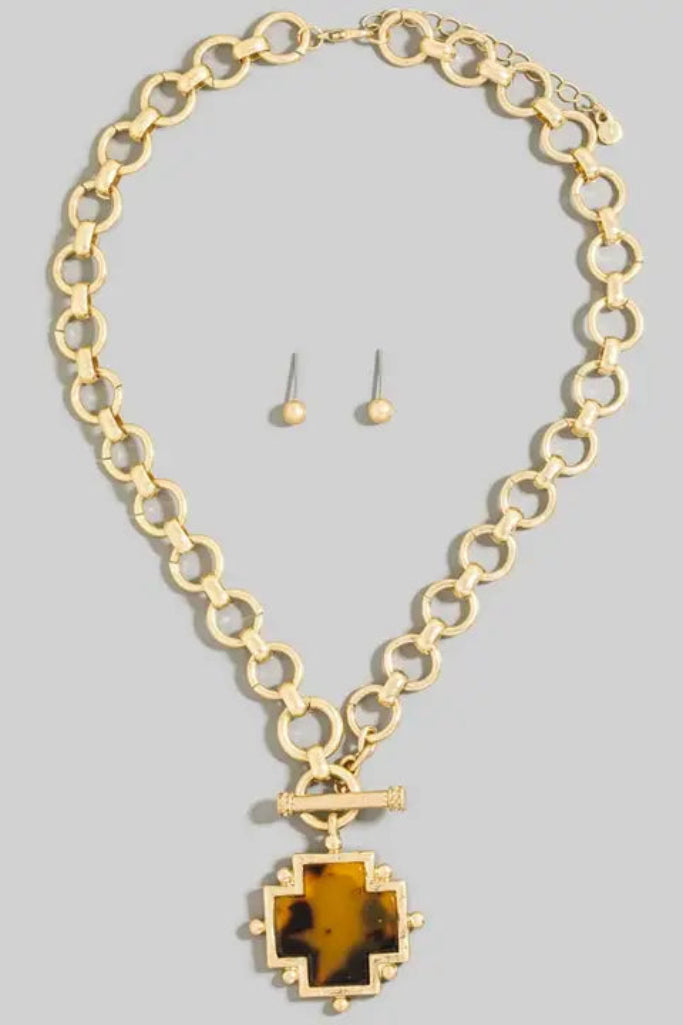 Gold necklace with a pendant and matching earrings on a gray background