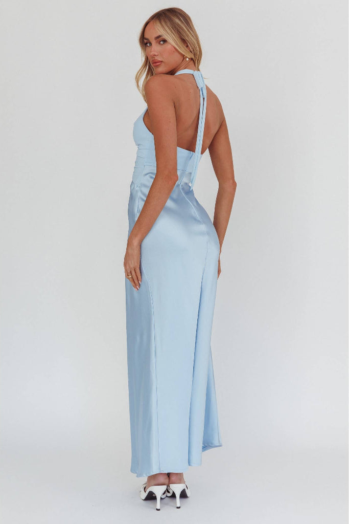A woman modeling a light blue satin maxi dress with a halter-style back and side cutout, shown from the back against a plain light gray studio background.