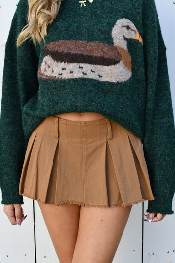 Front of mocha pleated mini skort with frayed hem worn with a green duck sweater
