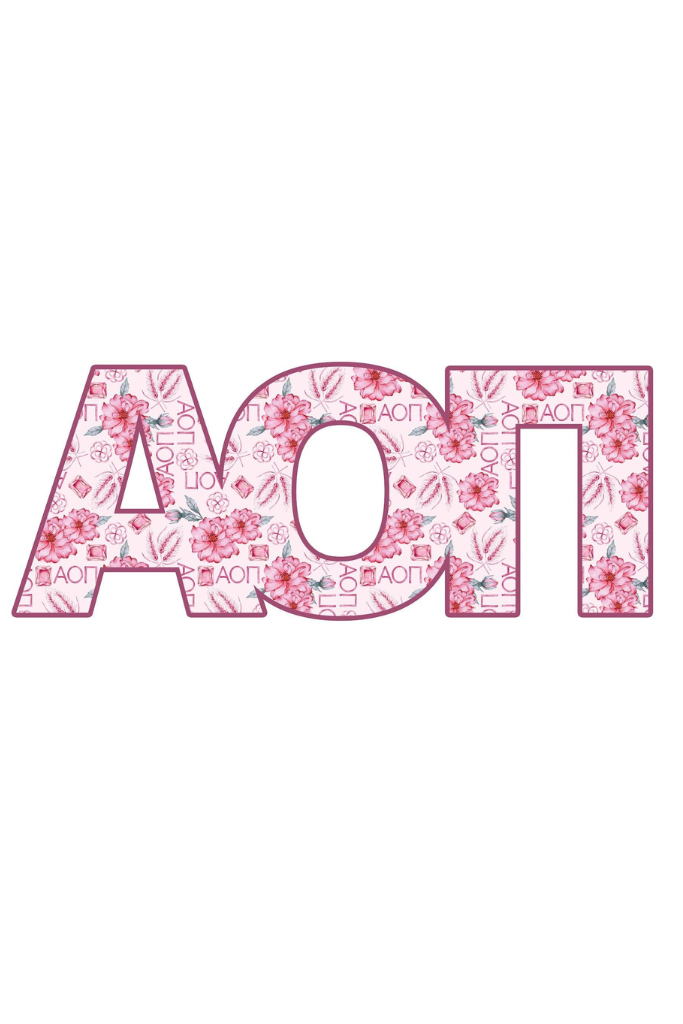 A smiling young woman in a white dress stands outdoors in a garden, holding up decorative pink letters spelling 'AOT' with a floral pattern.