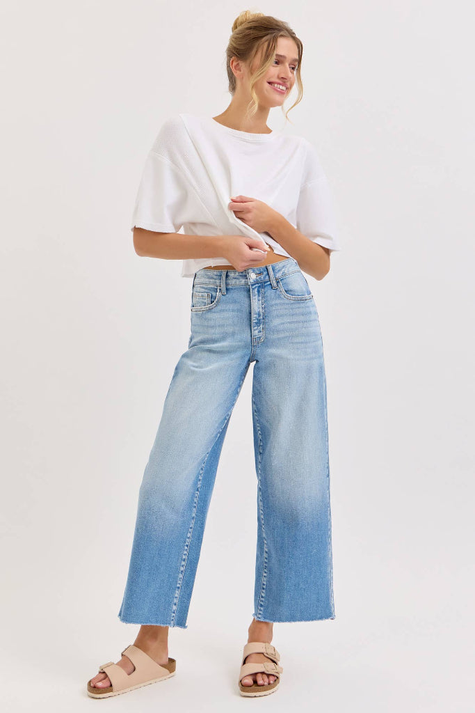Woman wearing a white cropped top and light blue jeans on a white background