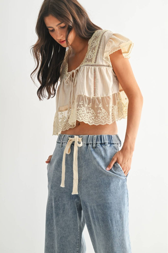 Woman wearing a lace top and blue pants on a white background