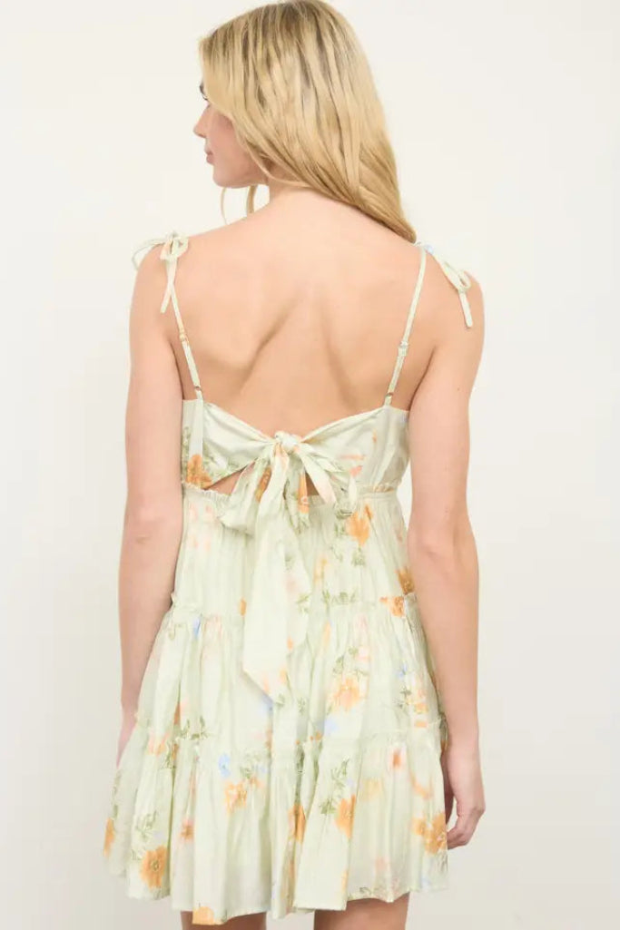 Woman wearing a light green floral dress with thin straps on a plain background