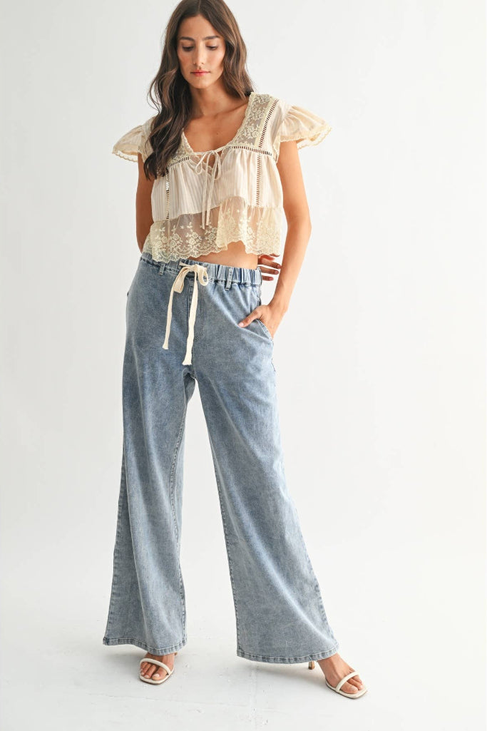 Woman wearing a lace top and wide-leg jeans on a white background