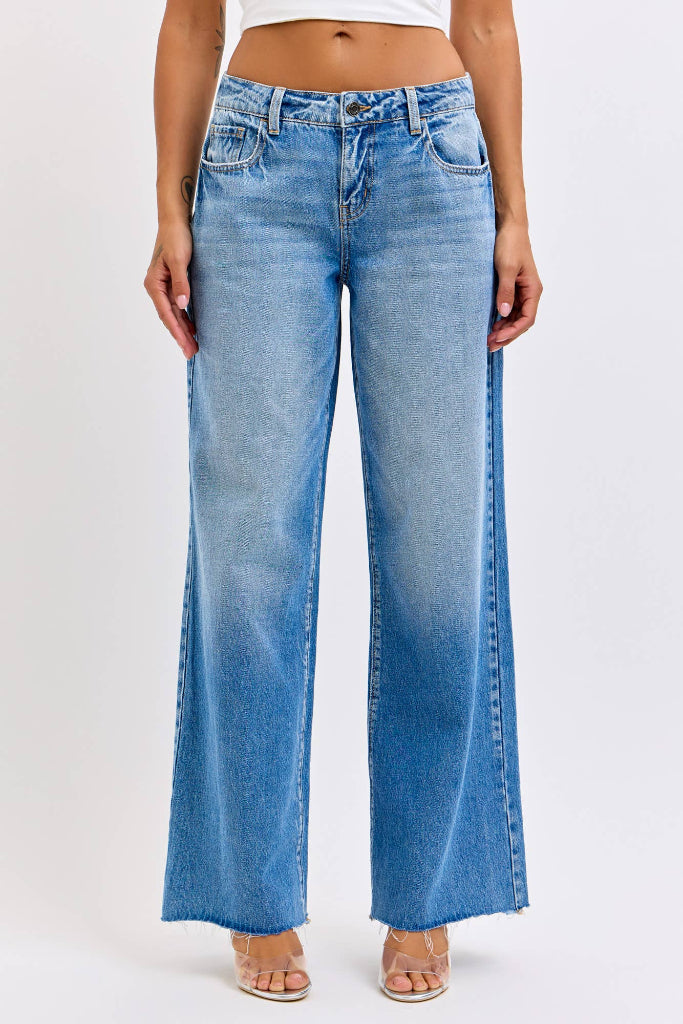 A model wearing a pair of light blue wide-leg denim jeans with a faded wash and side slit details, paired with a white crop top and clear high-heeled sandals against a plain white studio background.
