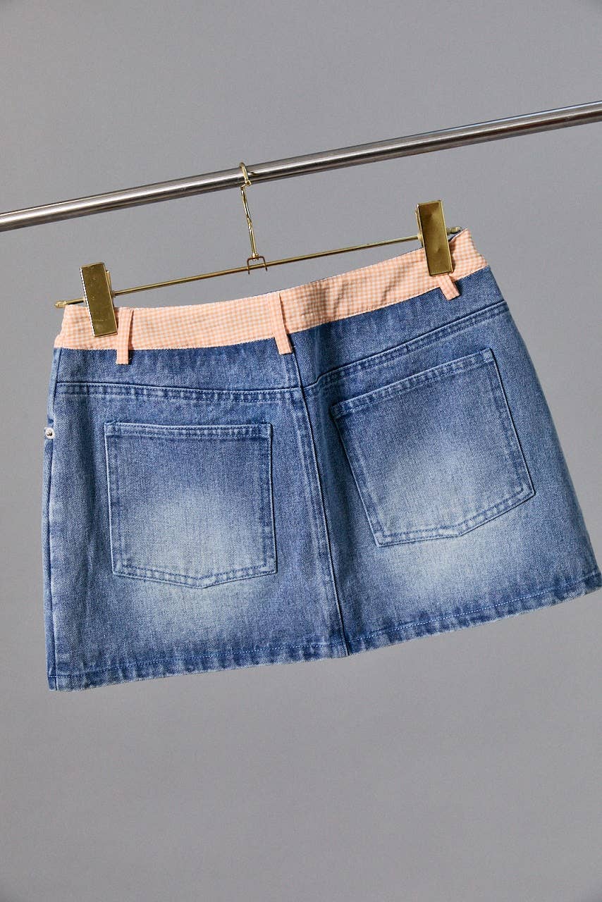 Blue denim skirt with a pink belt on a gray background