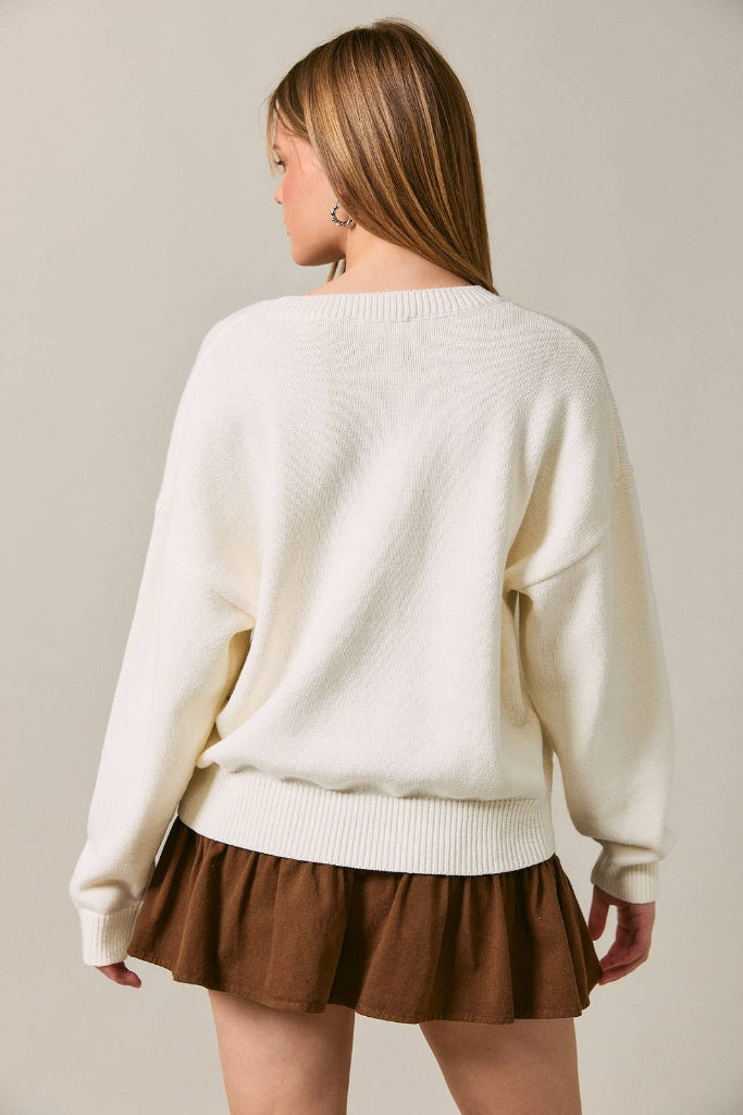 Woman wearing a cream sweater and brown skirt against a plain background