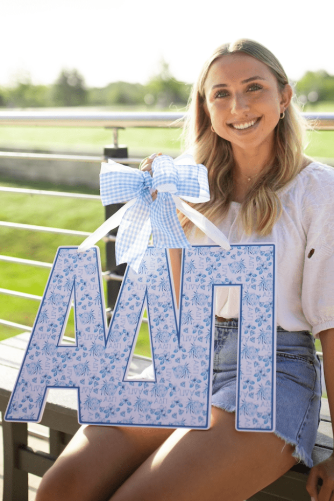 Woman holding decorative letters with a blue bow outdoors