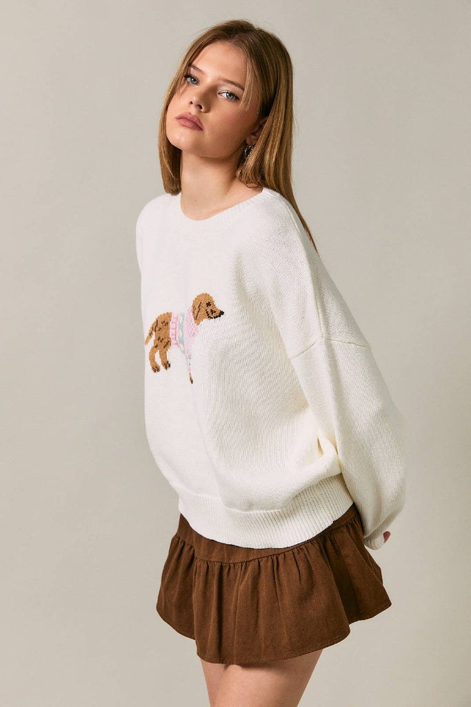 Woman wearing a white sweater with dog designs and brown shorts on a plain background
