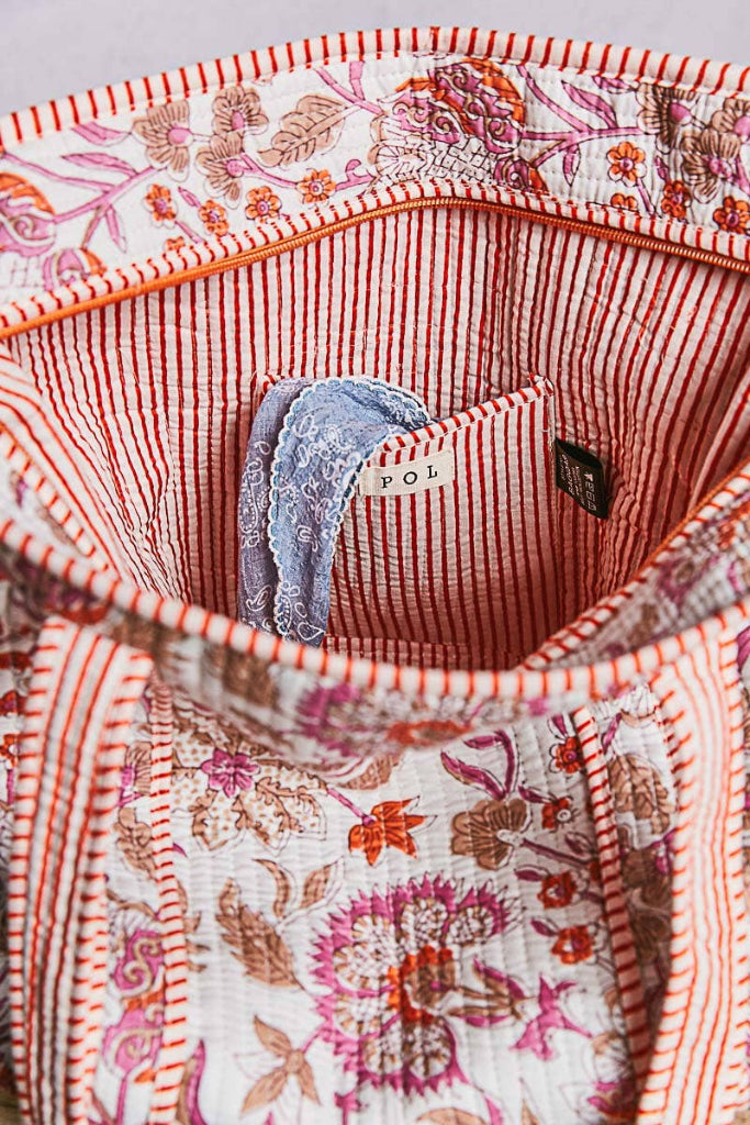 Close-up of a floral-patterned fabric with a pocket containing a blue item and visible branding.