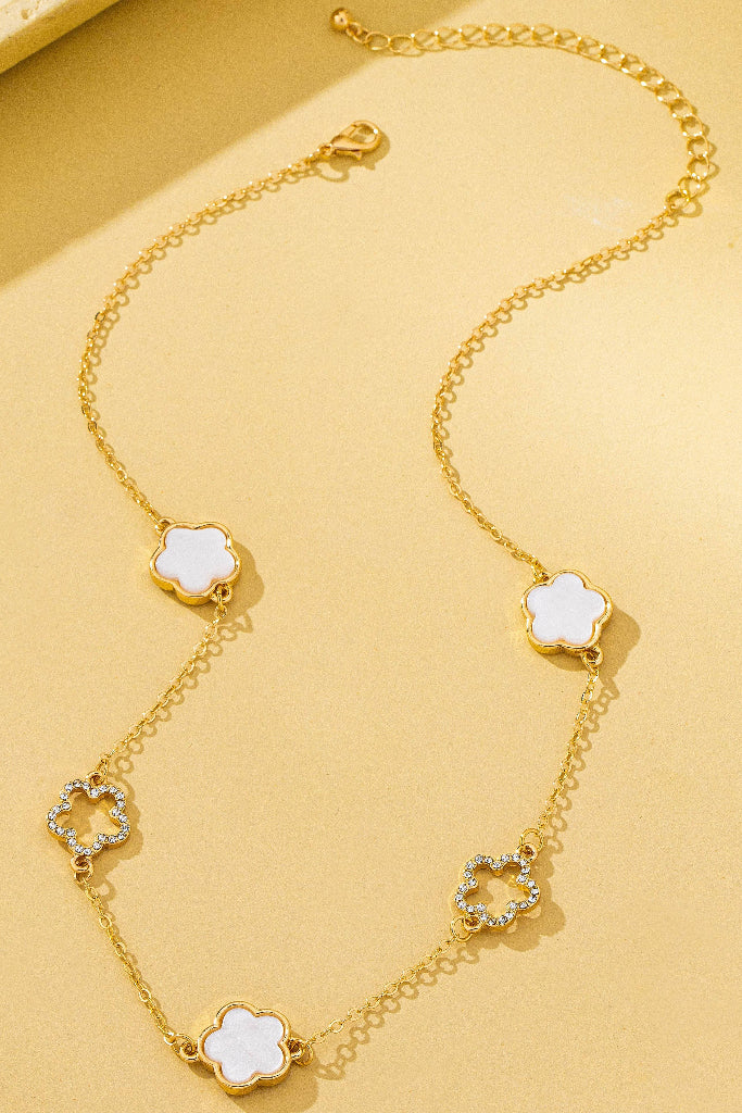 Gold necklace with clover-shaped pendants on a yellow background