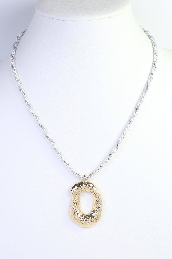 A textured gold oval pendant necklace on a twisted silver chain, displayed on a white mannequin bust.